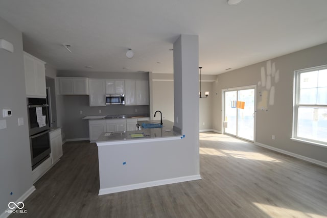 kitchen with stainless steel microwave, wood finished floors, multiple ovens, stovetop, and white cabinetry