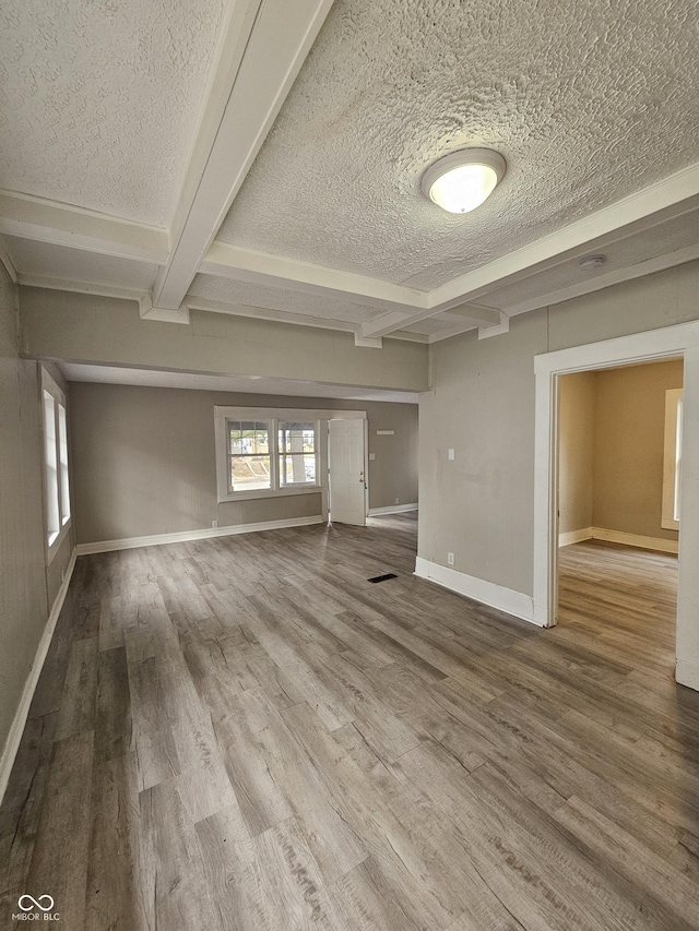 unfurnished living room featuring hardwood / wood-style flooring, a textured ceiling, and beamed ceiling