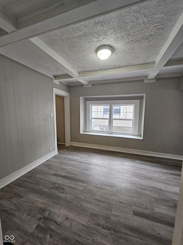 spare room featuring dark hardwood / wood-style flooring, a textured ceiling, and beamed ceiling