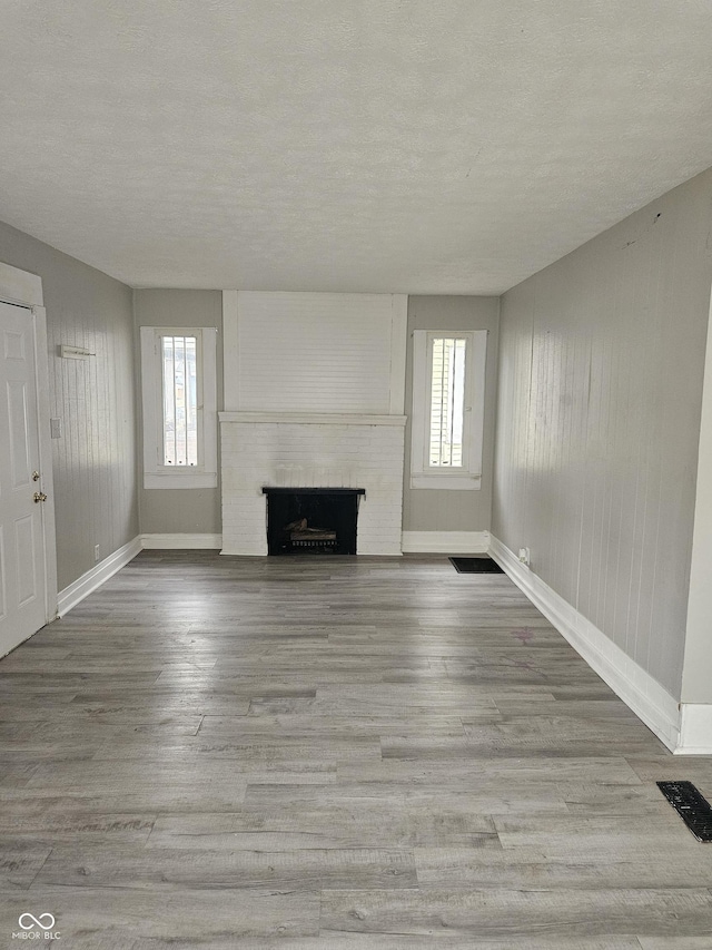 unfurnished living room featuring a fireplace, a textured ceiling, light hardwood / wood-style flooring, and a healthy amount of sunlight