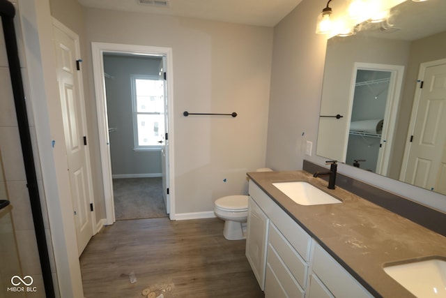 full bath featuring double vanity, toilet, a sink, wood finished floors, and baseboards