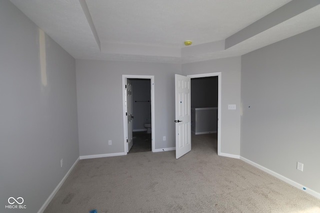 unfurnished bedroom with baseboards, a raised ceiling, ensuite bath, a spacious closet, and carpet floors