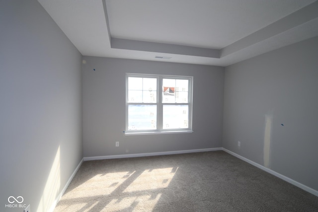 carpeted spare room featuring a tray ceiling, visible vents, and baseboards