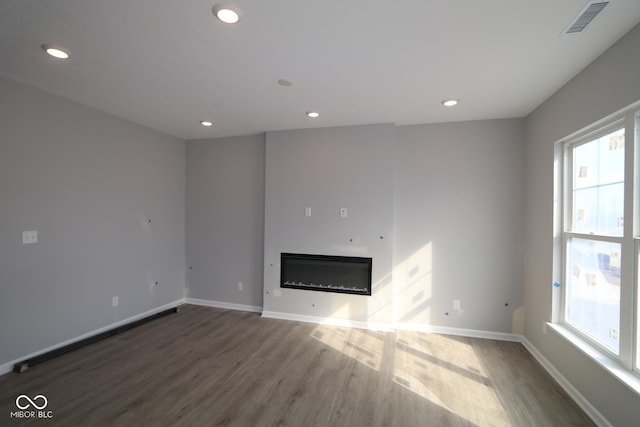 unfurnished living room featuring a glass covered fireplace, baseboards, recessed lighting, and wood finished floors