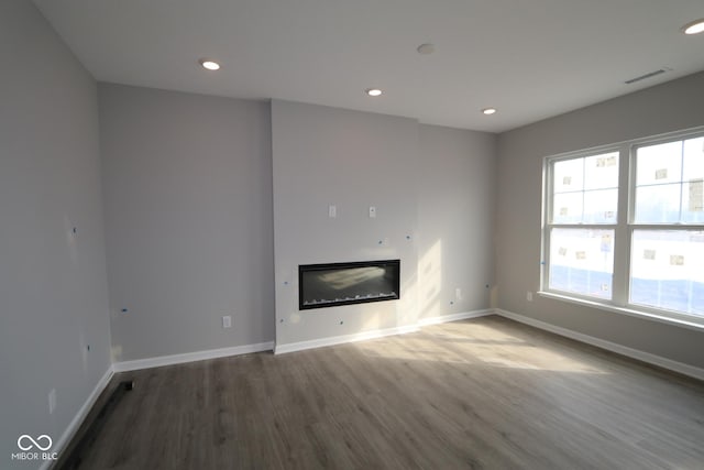 unfurnished living room featuring recessed lighting, baseboards, wood finished floors, and a glass covered fireplace