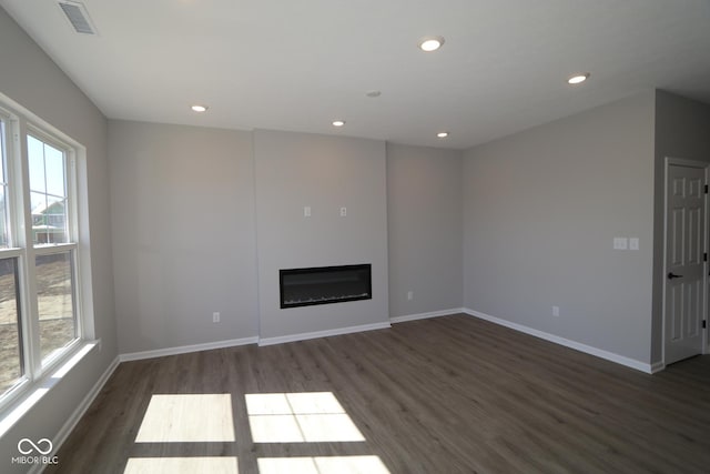 unfurnished living room featuring dark wood-style floors, visible vents, baseboards, recessed lighting, and a glass covered fireplace