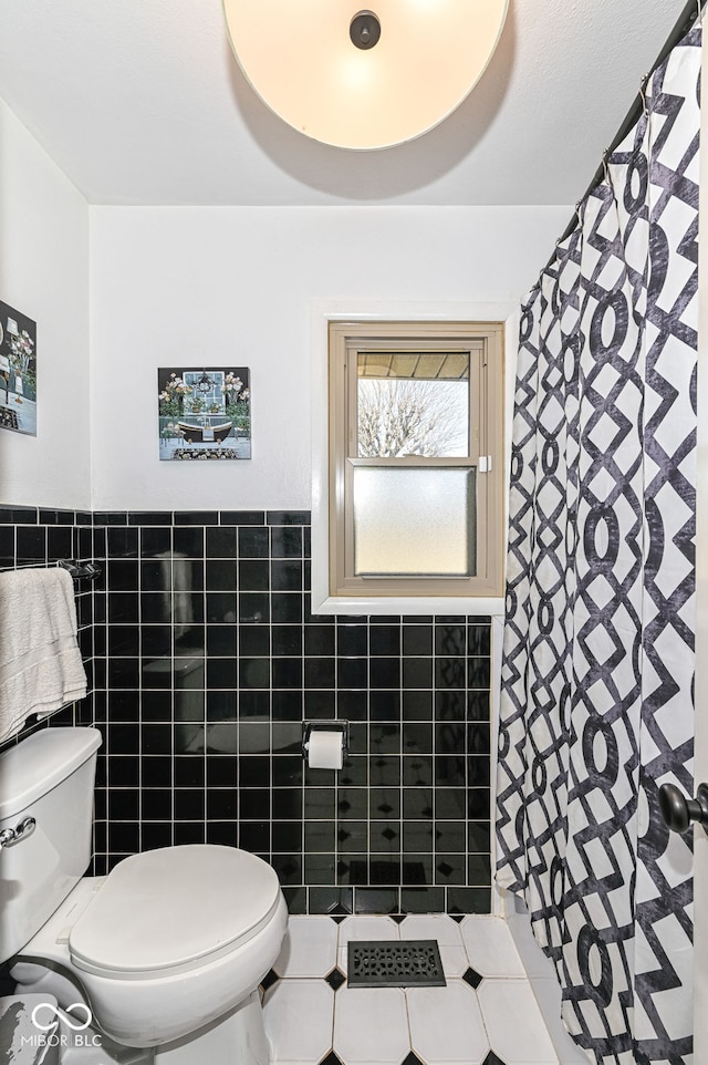 bathroom with toilet, tile patterned flooring, and tile walls