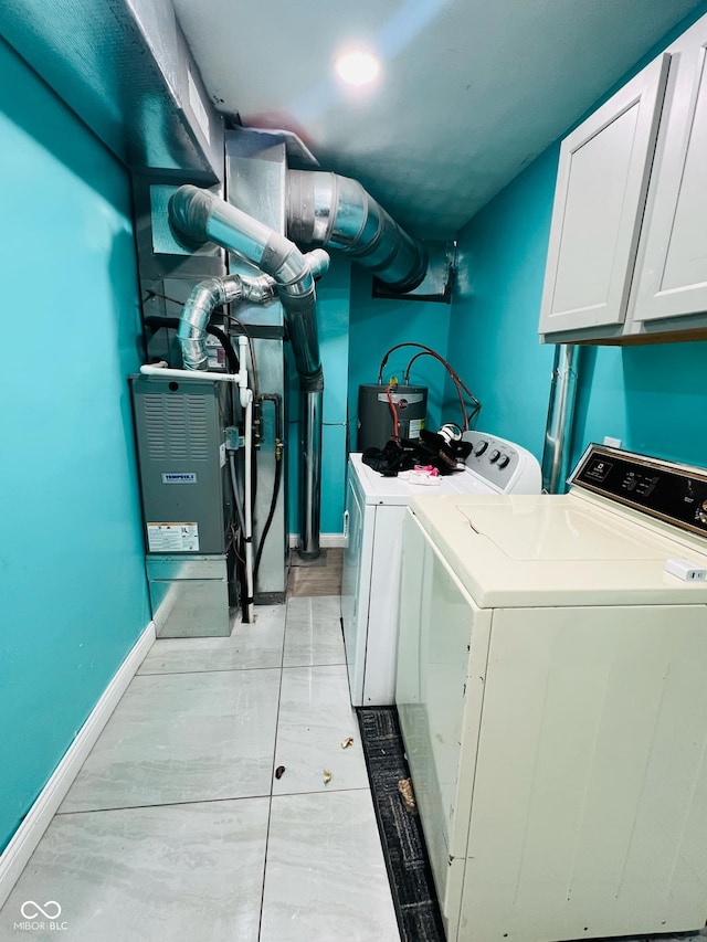 clothes washing area featuring water heater, washer and clothes dryer, and cabinets