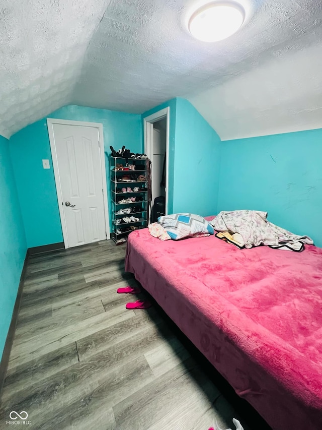 bedroom featuring vaulted ceiling, hardwood / wood-style floors, and a textured ceiling