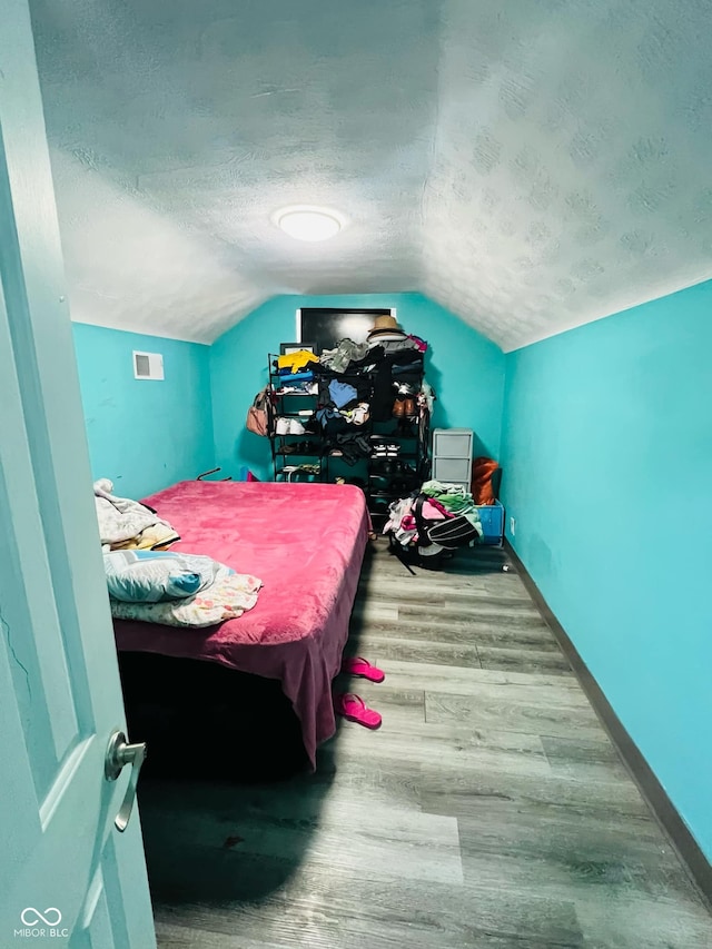 bedroom featuring vaulted ceiling, hardwood / wood-style floors, and a textured ceiling