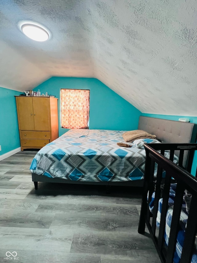 bedroom featuring wood-type flooring, vaulted ceiling, and a textured ceiling