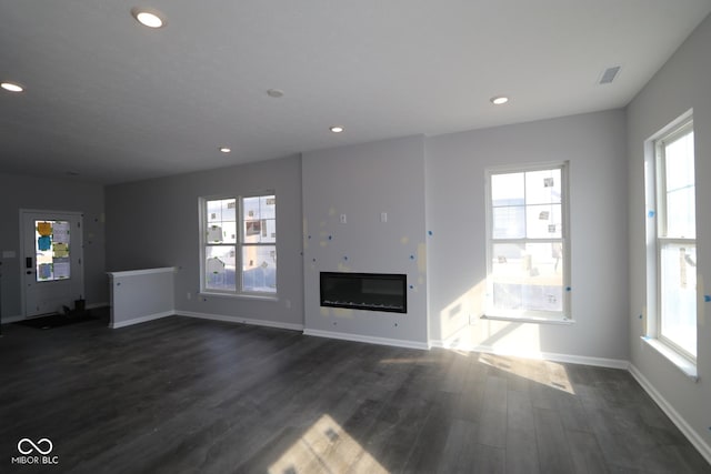 unfurnished living room featuring dark wood-style floors, baseboards, a glass covered fireplace, and recessed lighting