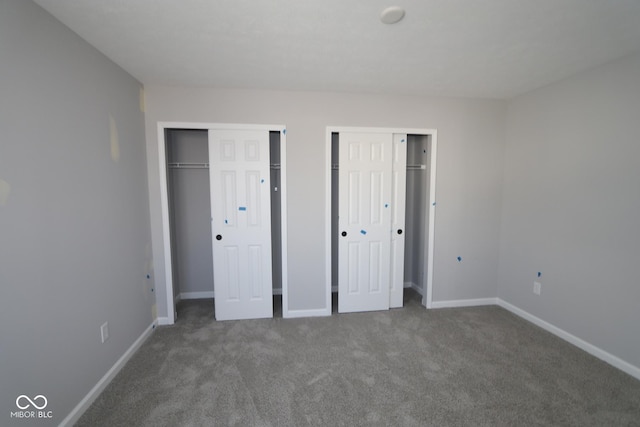 unfurnished bedroom featuring carpet flooring, baseboards, and two closets