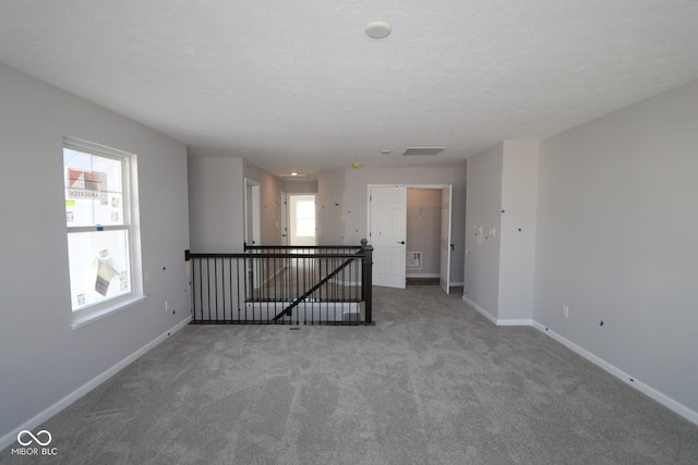 spare room featuring a textured ceiling, carpet, and baseboards