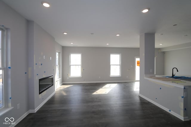 unfurnished living room with recessed lighting, baseboards, wood finished floors, and a glass covered fireplace