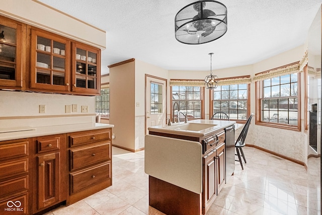 kitchen featuring glass insert cabinets, pendant lighting, light countertops, and brown cabinetry