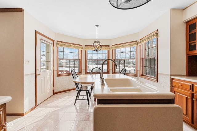 kitchen featuring light countertops, brown cabinets, a kitchen island with sink, and decorative light fixtures