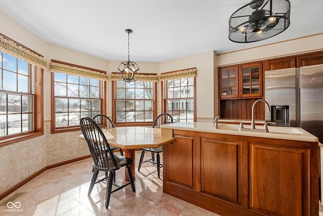 kitchen with brown cabinetry, glass insert cabinets, light countertops, and decorative light fixtures