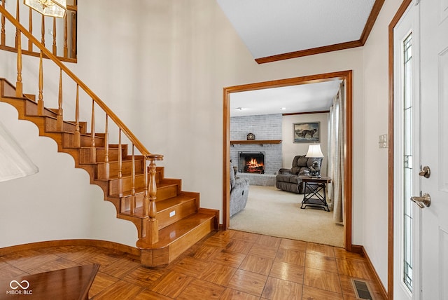 foyer entrance featuring crown molding, visible vents, stairway, a brick fireplace, and baseboards