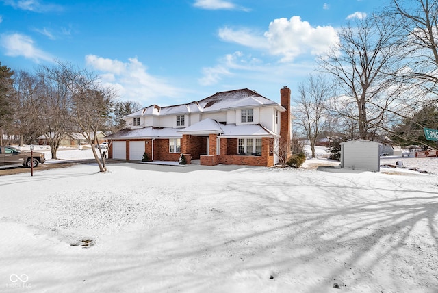 snow covered property featuring a garage, a chimney, and brick siding