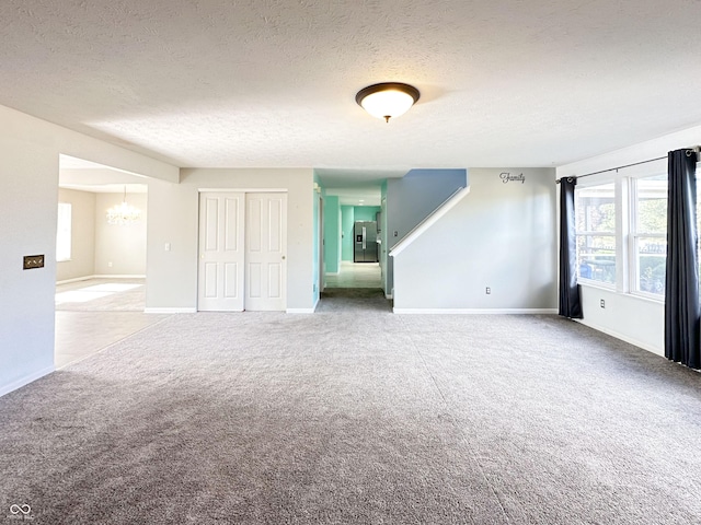 unfurnished room with carpet flooring, a notable chandelier, and a textured ceiling