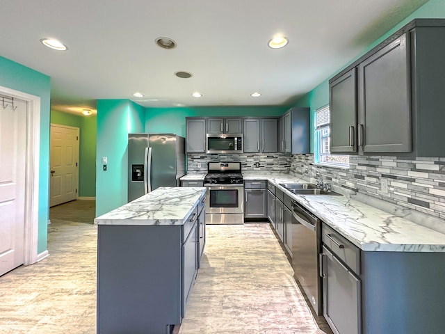 kitchen featuring sink, gray cabinets, appliances with stainless steel finishes, a center island, and tasteful backsplash