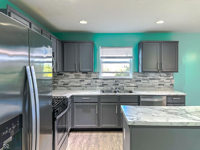 kitchen featuring sink, gray cabinetry, stainless steel appliances, light hardwood / wood-style floors, and decorative backsplash