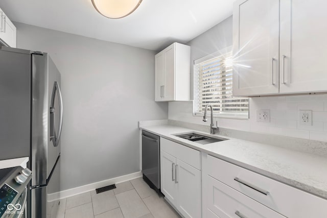 kitchen with appliances with stainless steel finishes, sink, white cabinets, backsplash, and light tile patterned floors