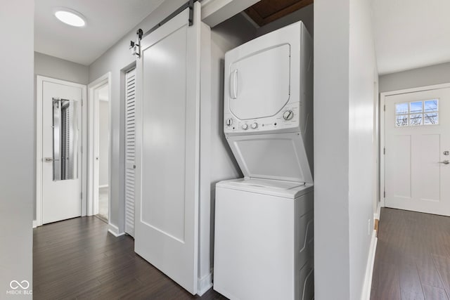 clothes washing area with stacked washing maching and dryer, a barn door, and dark wood-type flooring