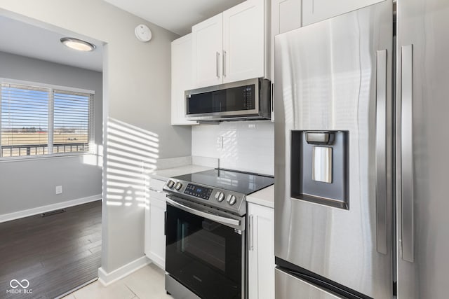 kitchen featuring appliances with stainless steel finishes, light wood-type flooring, white cabinets, and backsplash