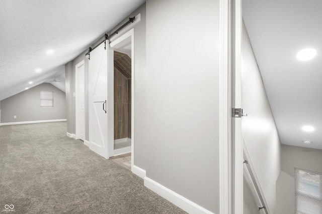 corridor featuring light carpet, vaulted ceiling, a barn door, and a textured ceiling