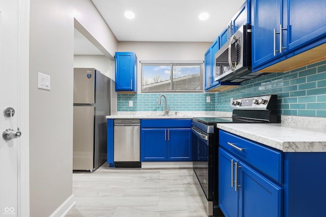 kitchen featuring blue cabinets, sink, light wood-type flooring, appliances with stainless steel finishes, and backsplash