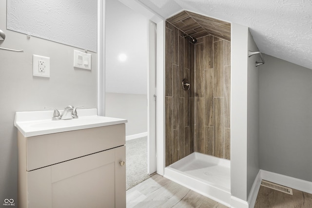 bathroom with hardwood / wood-style flooring, vanity, lofted ceiling, and a tile shower