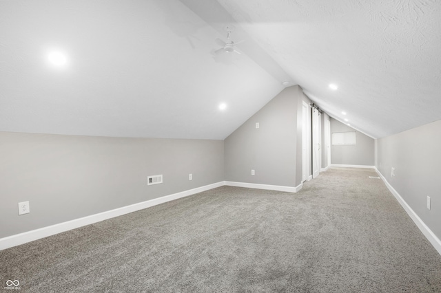 additional living space featuring ceiling fan, vaulted ceiling, a textured ceiling, and carpet