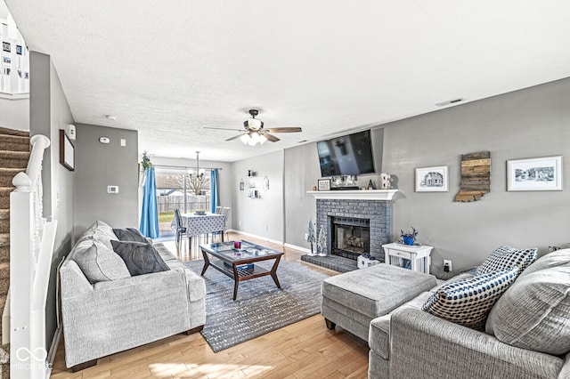 living room featuring a brick fireplace, hardwood / wood-style flooring, ceiling fan with notable chandelier, and a textured ceiling