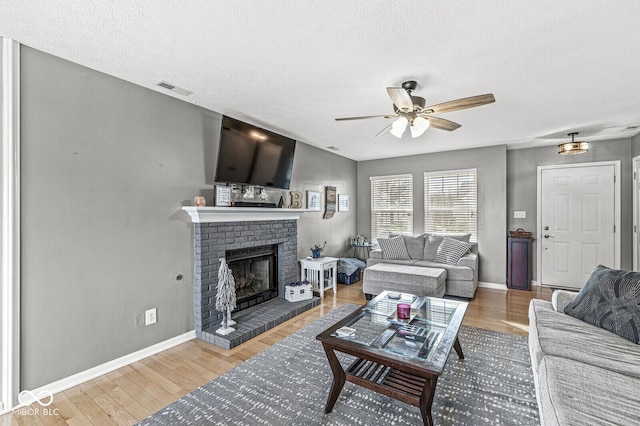 living room featuring hardwood / wood-style flooring, a brick fireplace, a textured ceiling, and ceiling fan