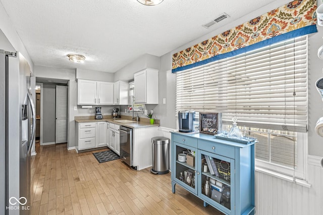 kitchen featuring appliances with stainless steel finishes, white cabinetry, sink, a textured ceiling, and light hardwood / wood-style flooring