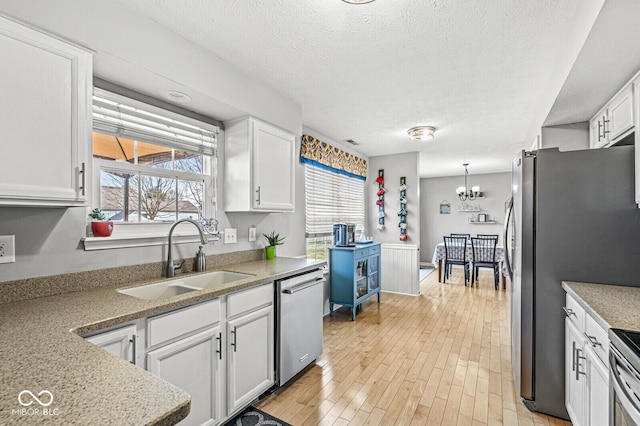 kitchen featuring sink, white cabinetry, a textured ceiling, a notable chandelier, and stainless steel appliances