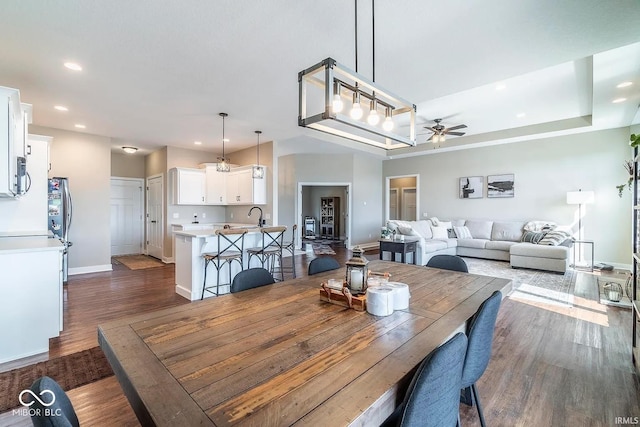 dining space with dark hardwood / wood-style flooring, sink, a raised ceiling, and ceiling fan