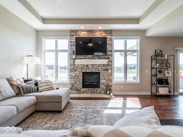 living room with hardwood / wood-style flooring, a raised ceiling, and a stone fireplace