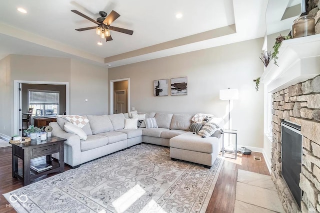 living room featuring hardwood / wood-style floors, a fireplace, ceiling fan, and a tray ceiling