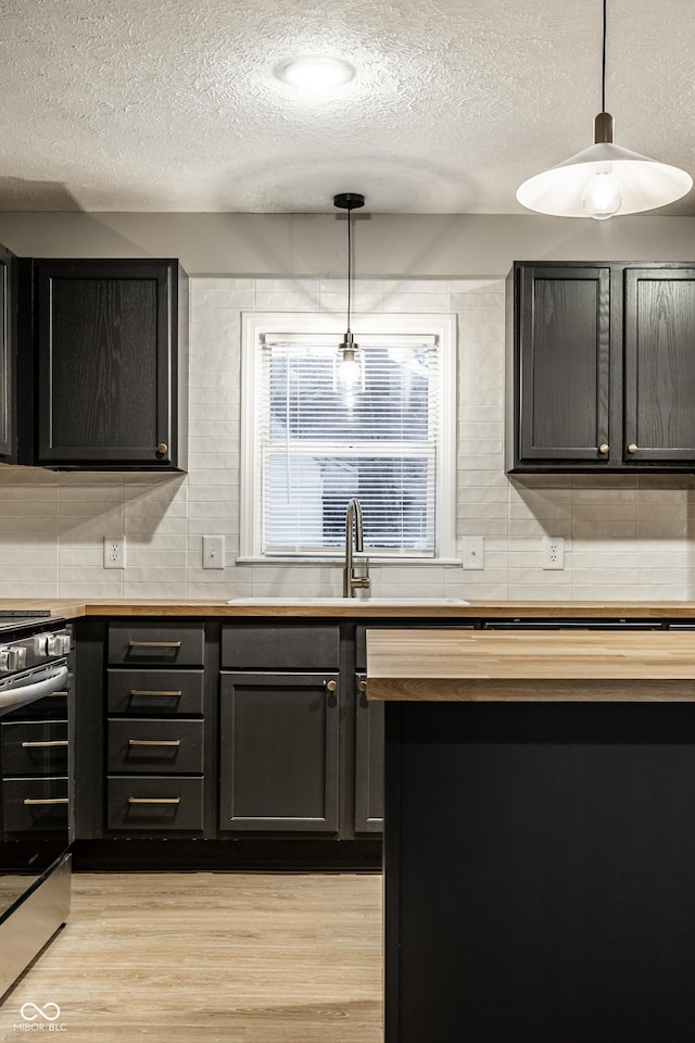 kitchen with hanging light fixtures, decorative backsplash, light hardwood / wood-style flooring, and stainless steel range oven