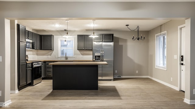 kitchen with sink, decorative light fixtures, appliances with stainless steel finishes, a kitchen island, and light hardwood / wood-style floors