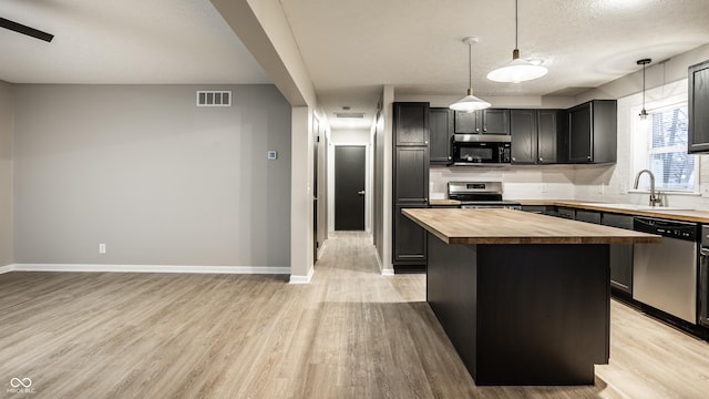 kitchen with pendant lighting, backsplash, stainless steel appliances, a kitchen island, and wood counters