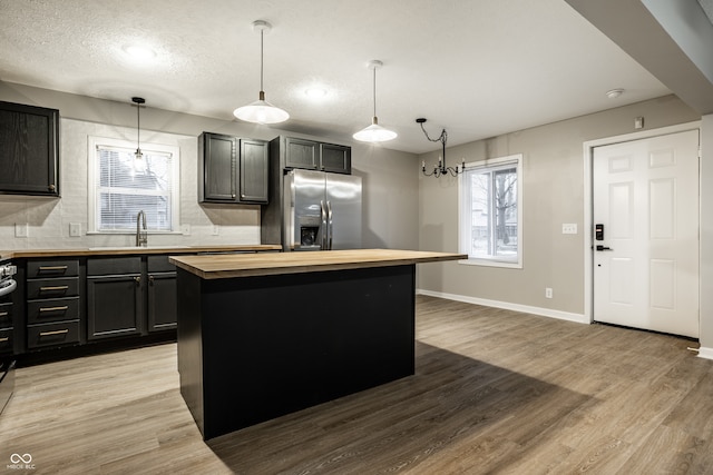 kitchen featuring a kitchen island, decorative light fixtures, sink, wooden counters, and stainless steel fridge with ice dispenser