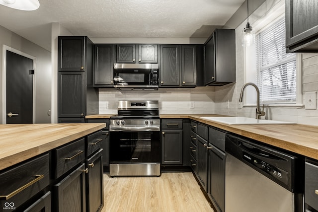 kitchen featuring pendant lighting, sink, appliances with stainless steel finishes, butcher block counters, and decorative backsplash