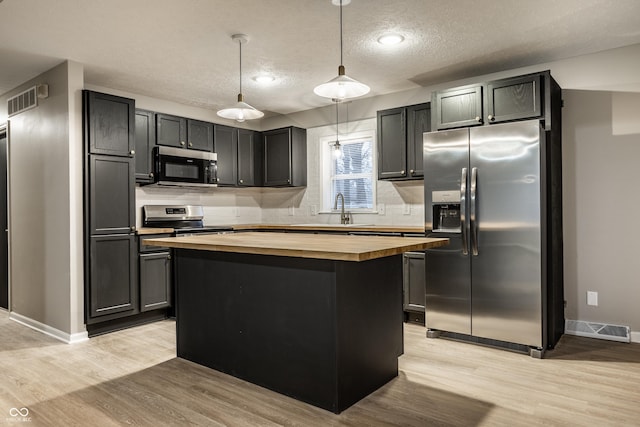 kitchen featuring butcher block countertops, stainless steel appliances, a center island, light hardwood / wood-style floors, and decorative light fixtures