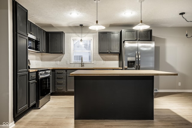 kitchen with stainless steel appliances, a kitchen island, wood counters, and decorative light fixtures