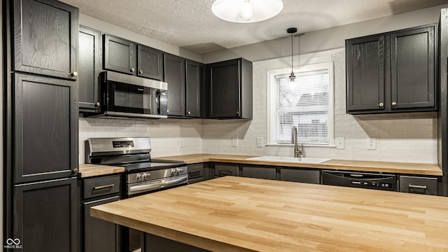 kitchen with pendant lighting, sink, butcher block counters, backsplash, and stainless steel appliances