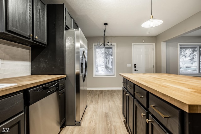 kitchen featuring tasteful backsplash, appliances with stainless steel finishes, butcher block counters, and hanging light fixtures